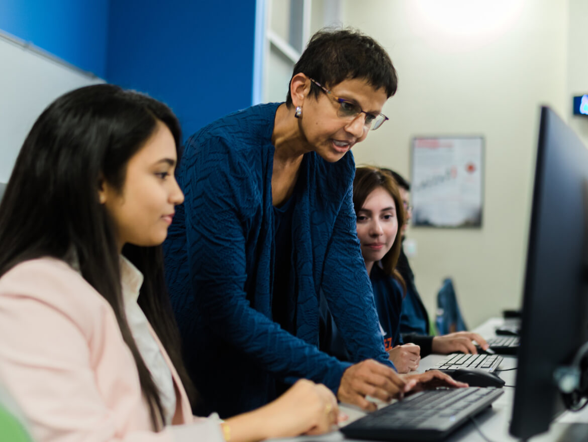 Female professor touching the computer keyboard while her students look on.
