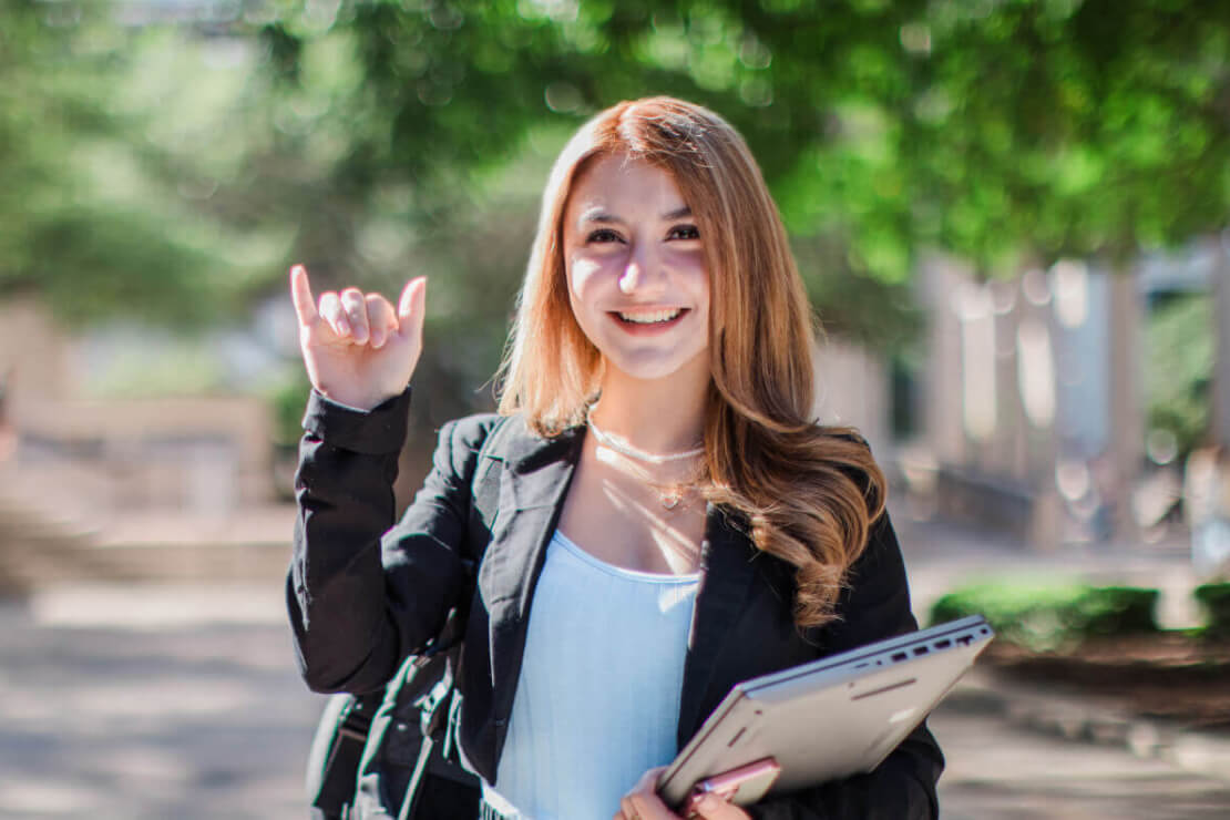 UTSA Student holding her laptop and making a Bird's Up hand signal