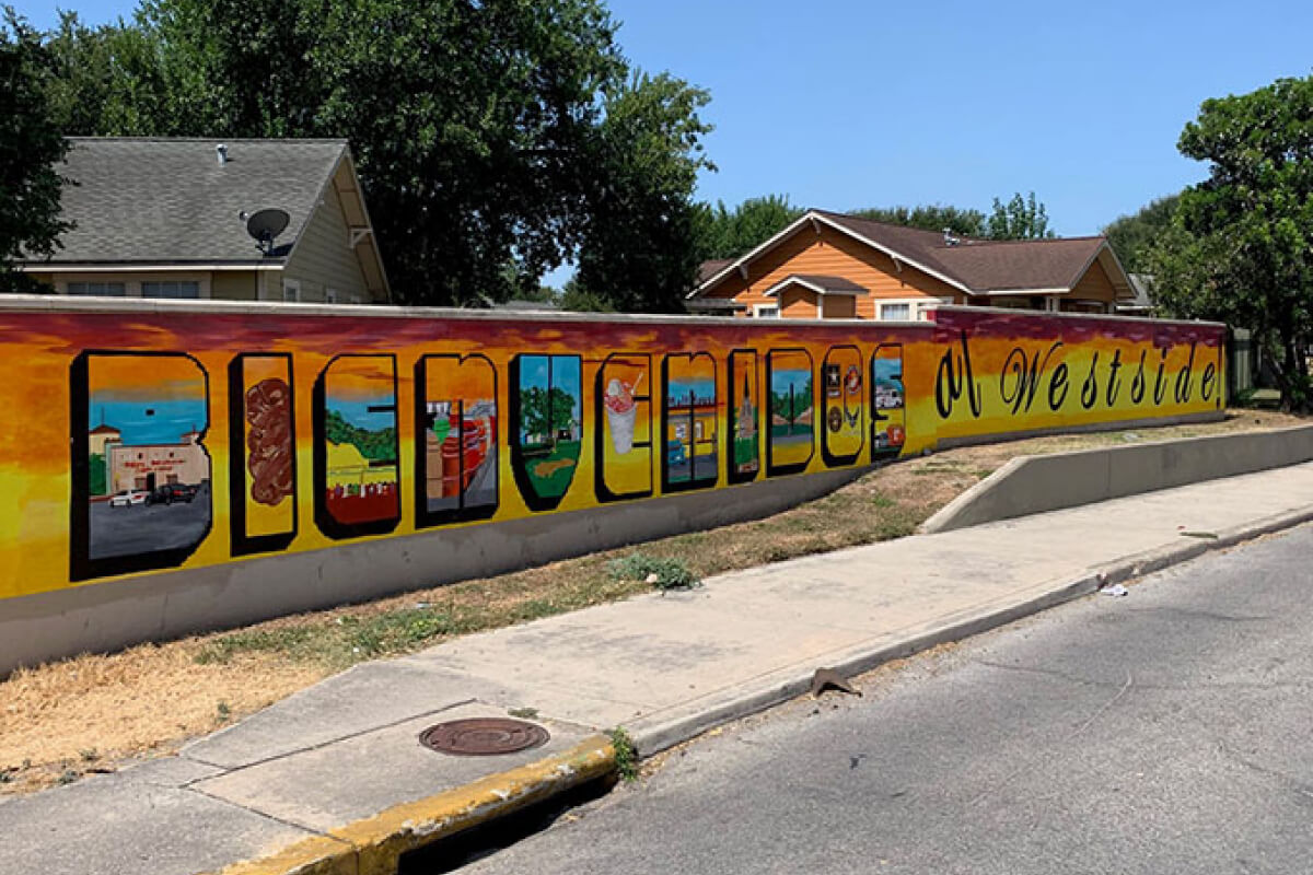 A concrete fence with a mural that says 'Bienvenidos al Westside', which in means 'Welcome to the Westside'. 