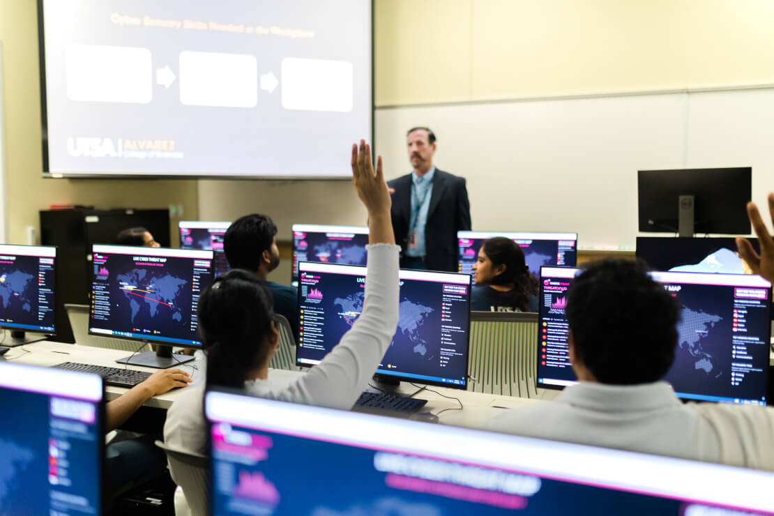 Student sitting in front of a desktop computer with instructor looking at him.
