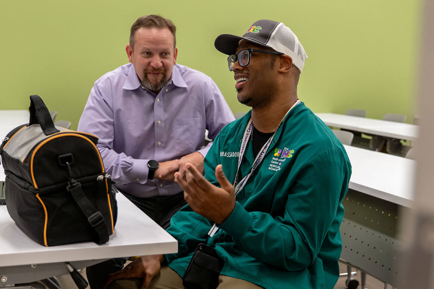 Two guys talking at a table inside a classroom